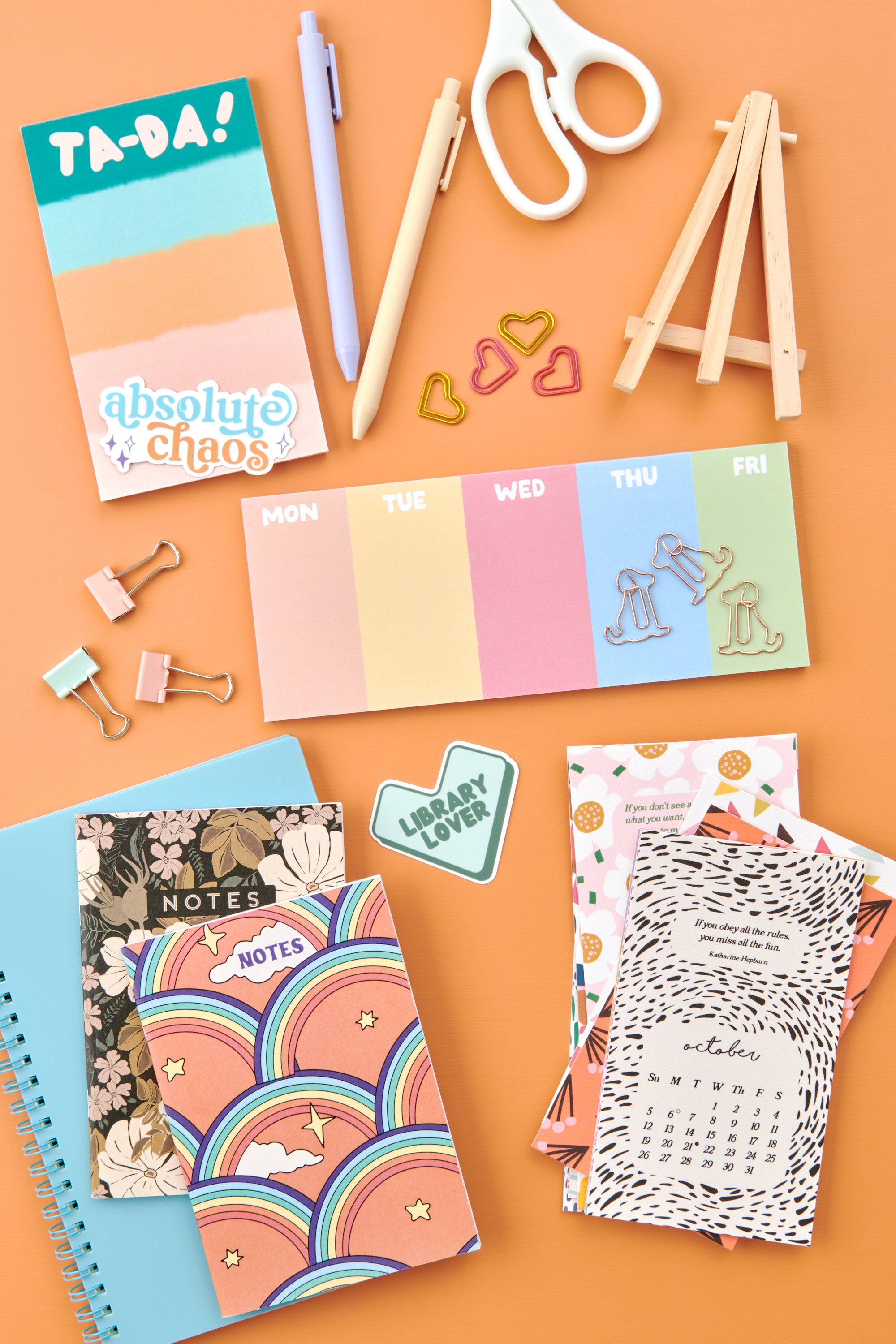 Assorted stationery items including notebooks, stickers, and office supplies on an orange background